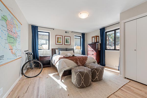 home-restoration-service A bright bedroom with a bed, two patterned ottomans, wooden furniture, blue curtains, a large world map on the wall, and a bicycle leaning against the wall on a hardwood floor.